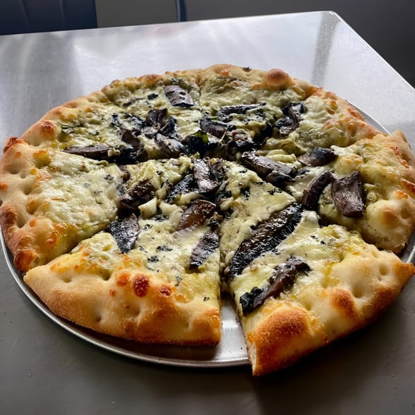 A Coastal Pizza Kitchen mushroom and white cheese pizza with one slice removed, on a metal tray.