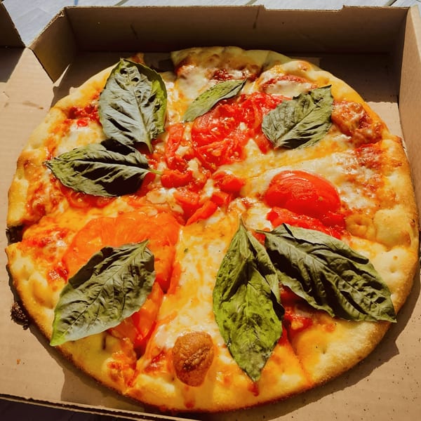 Coastal Pizza Kitchen's Margherita pizza with fresh basil and tomatoes in a cardboard box.