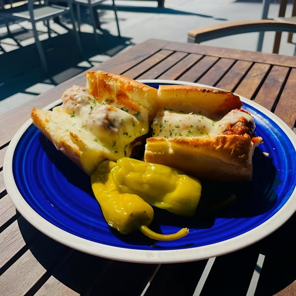 Meatball sub sandwiches with melted cheese and banana peppers on a blue plate on a wooden table.
