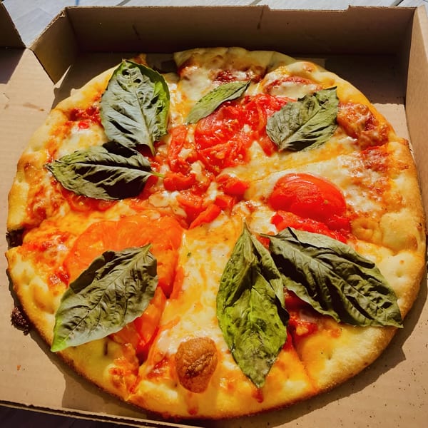 Coastal Pizza Kitchen's Margherita pizza with fresh basil leaves and diced tomatoes in a cardboard box.