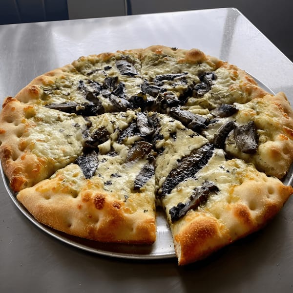 Coastal Pizza Kitchen's white pizza with mushrooms and a thick, bubbly crust on a metal tray.