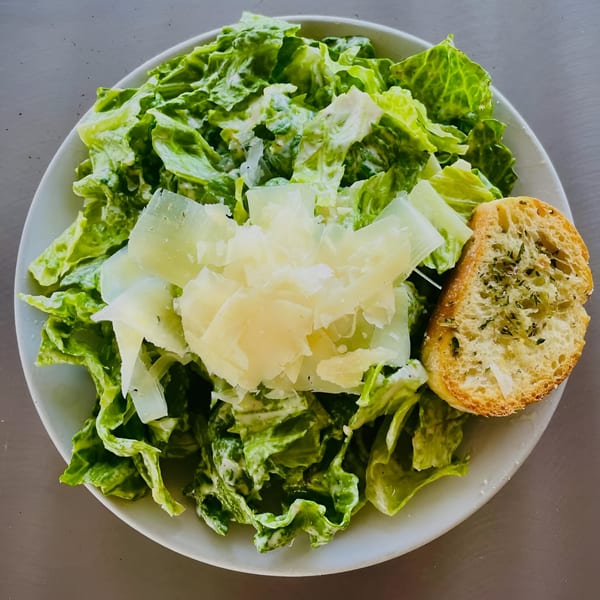 A fresh Caesar salad with shaved Parmesan cheese and a side of garlic bread.