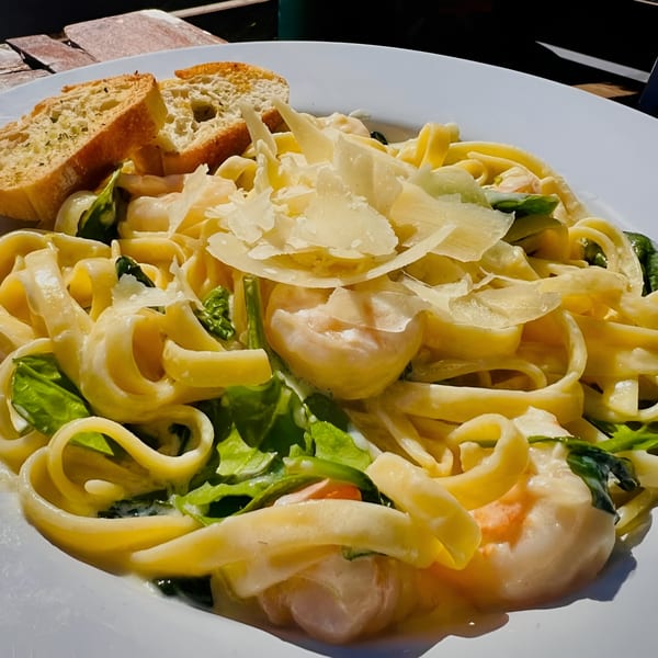 Creamy shrimp fettuccine pasta with spinach, parmesan, and garlic bread on a white plate.