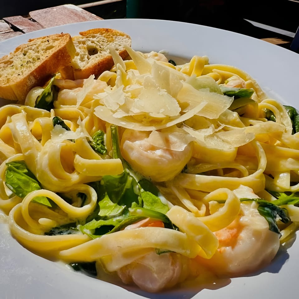 Creamy shrimp fettuccine pasta with spinach, parmesan, and garlic bread on a white plate.
